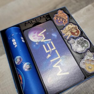 Peut inclure: Une bo&icirc;te de jeu de soci&eacute;t&eacute; bleue et dor&eacute;e avec le titre "Meow Meow" sur le couvercle. La bo&icirc;te contient un plateau de jeu bleu, un gobelet &agrave; d&eacute;s bleu et cinq pions sur le th&egrave;me des chats.