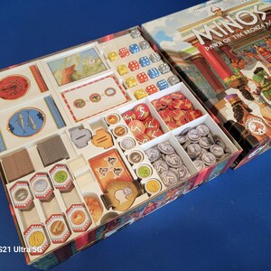 Puede incluir: Un inserto organizador blanco con compartimentos para guardar piezas de juego, dados y cartas. El inserto está diseñado para el juego de mesa "Minos: Dawn of the Bronze Age".