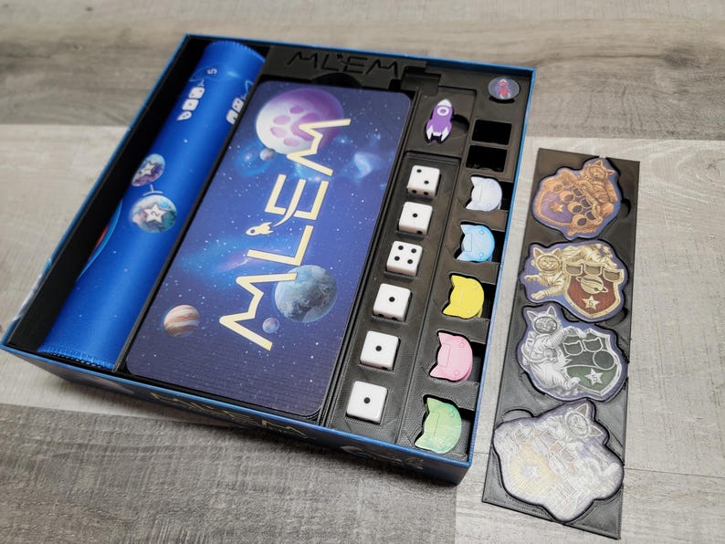 Peut inclure: Une bo&icirc;te de jeu bleue avec un design sur le th&egrave;me de l'espace. La bo&icirc;te contient des d&eacute;s, des jetons et un plateau de jeu. Le plateau de jeu pr&eacute;sente un design de galaxie avec le mot "MILLEM" imprim&eacute; dessus. La bo&icirc;te comprend &eacute;galement un ensemble de jetons color&eacute;s avec des personnages ressemblant &agrave; des chats.