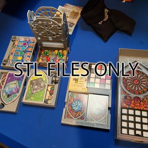 Puede incluir: Un organizador de juegos impreso en 3D para el juego de mesa "Stained Glass of the Stained Glass of the Saints". El organizador incluye compartimentos para los componentes del juego, incluidos dados, cartas y fichas. El organizador está hecho de plástico gris claro y tiene un diseño de vitral.