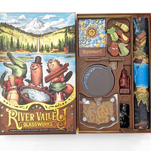 May include: A board game box and its contents are shown. The box art depicts cartoon animals in a river scene. Inside, the game includes cards, tokens, and a game board. The game is titled "River Valle Glassworks."