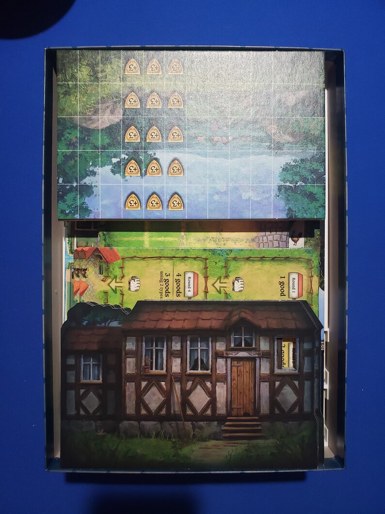 May include: A board game box with various game components. The box contains a game board with a landscape scene, wooden tokens, and cards. A detailed illustration of a house is visible. The game appears to be a strategy or resource management game.