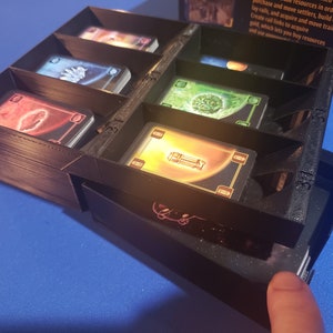 May include: A black plastic organizer with multiple compartments for storing cards. The organizer has a drawer that slides out to reveal more storage space. The organizer is labeled with numbers.