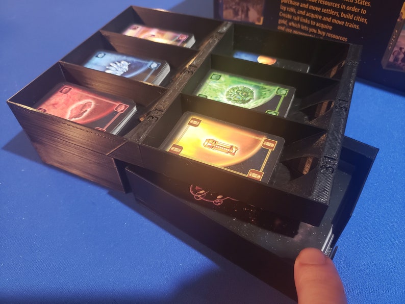 May include: A black plastic organizer with multiple compartments for storing cards. The organizer has a drawer that slides out to reveal more storage space. The organizer is labeled with numbers.