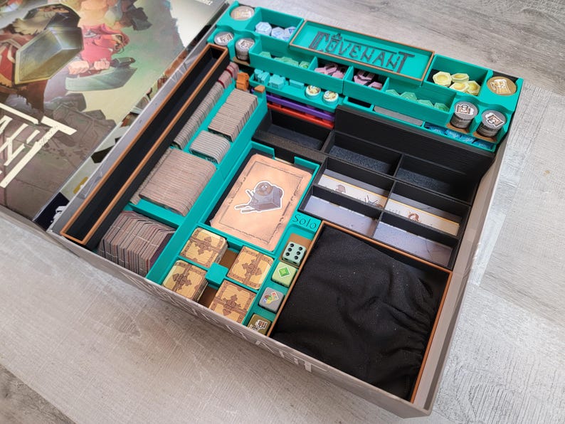 May include: A board game organizer with teal and black compartments. The organizer holds cards, tokens, dice, and other game components. The game box is open, revealing the organized interior. The word "COVENANT" is visible.