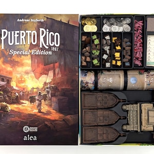 May include: The board game "Puerto Rico 1897 Special Edition" is shown open, displaying game components. The box art features a harbour scene. Inside, there are tokens, cards, and miniature ships, all neatly organised in a black tray.