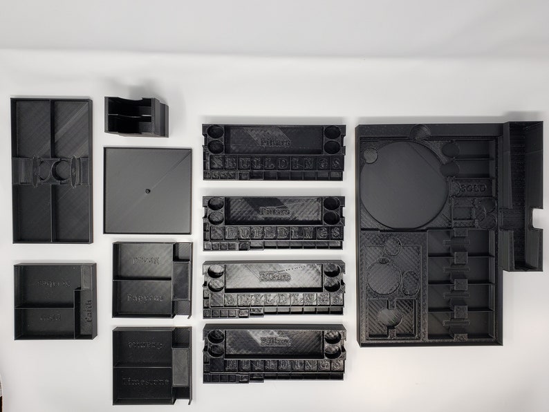 May include: A set of 10 black plastic storage containers with various compartments and labels. The containers are designed to organize and store small items, such as dice, tokens, and cards.