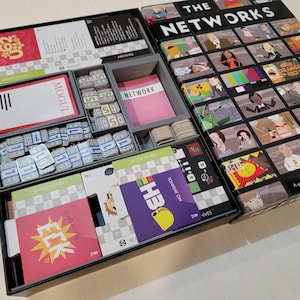 May include: Board game box titled "THE NETWORKS" with game components visible. Includes cards, play money, and game pieces. The box art features a grid of illustrated characters. The game includes the text "MOGUL" and "NETWORK".