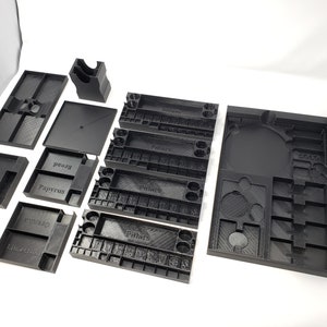 May include: A set of black plastic organizers for board games. The organizers are labeled with the names "Pillars", "Papyrus", "Bread", "Egusito", "Ankh", and "Solo".