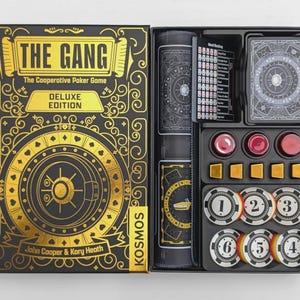Puede incluir: Juego de póquer cooperativo The Gang Deluxe Edition con una caja de diseño de caja fuerte en negro y oro. La caja abierta contiene una baraja de cartas, una tarjeta de referencia de manos, tres fichas rojas, cinco cubos dorados y seis fichas numeradas.