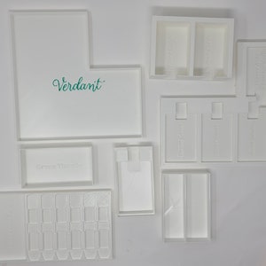 Puede incluir: Cajas de almacenamiento de pl&aacute;stico blanco con las palabras "Verdant", "Green Thumbs", "Fragrances", "Your Soft", "Soft Cash" y "Green Thumbs" impresas en ellas. Las cajas est&aacute;n dise&ntilde;adas para guardar objetos peque&ntilde;os como joyas, art&iacute;culos de artesan&iacute;a u otros objetos peque&ntilde;os.