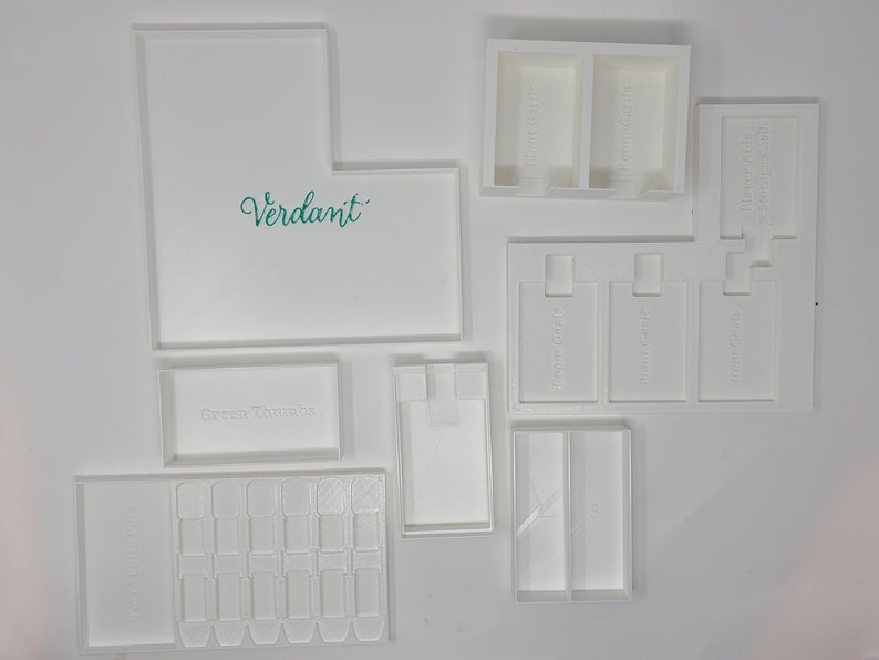 Puede incluir: Cajas de almacenamiento de pl&aacute;stico blanco con las palabras "Verdant", "Green Thumbs", "Fragrances", "Your Soft", "Soft Cash" y "Green Thumbs" impresas en ellas. Las cajas est&aacute;n dise&ntilde;adas para guardar objetos peque&ntilde;os como joyas, art&iacute;culos de artesan&iacute;a u otros objetos peque&ntilde;os.