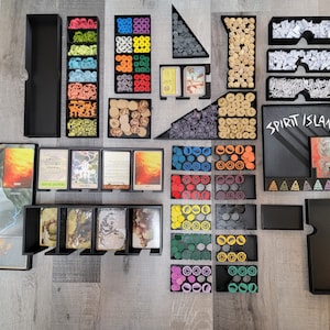 Puede incluir: Un organizador de juego de mesa Spirit Island con múltiples compartimentos para guardar los componentes del juego. El organizador incluye compartimentos para cartas, fichas y otras piezas de juego. El organizador está hecho de plástico negro y tiene un diseño elegante y moderno.
