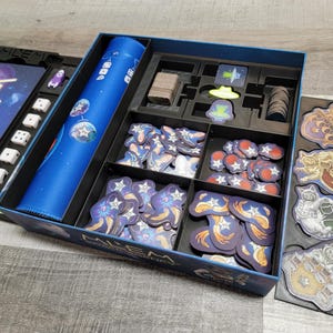 Peut inclure: Une bo&icirc;te de jeu bleue et noire avec un insert bleu pour ranger les pi&egrave;ces du jeu. La bo&icirc;te porte l'inscription "ALIEN" sur le couvercle. L'insert comporte des compartiments pour ranger diff&eacute;rents types de pi&egrave;ces de jeu, notamment des d&eacute;s, des jetons et des cartes.