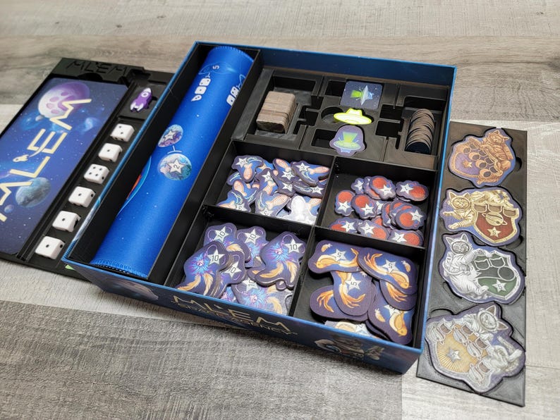 Peut inclure: Une bo&icirc;te de jeu bleue et noire avec un insert bleu pour ranger les pi&egrave;ces du jeu. La bo&icirc;te porte l'inscription "ALIEN" sur le couvercle. L'insert comporte des compartiments pour ranger diff&eacute;rents types de pi&egrave;ces de jeu, notamment des d&eacute;s, des jetons et des cartes.
