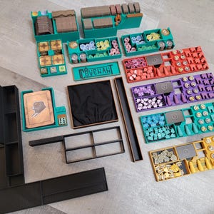 May include: An assortment of teal, black, red, purple, and yellow game organizers and components. The teal organizers have compartments for game pieces. The word "COVENANT" is printed on a teal sign. Various game pieces are visible.
