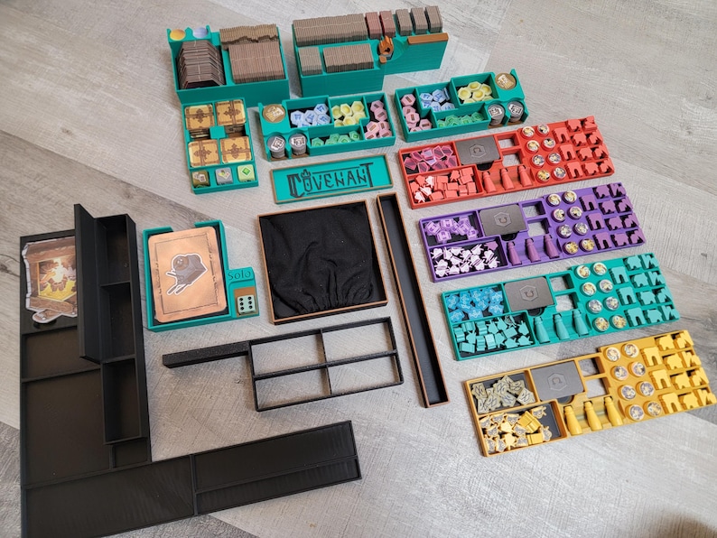 May include: An assortment of teal, black, red, purple, and yellow game organizers and components. The teal organizers have compartments for game pieces. The word "COVENANT" is printed on a teal sign. Various game pieces are visible.