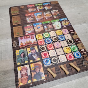 Puede incluir: Un tablero de juego con fondo de madera y fichas de colores. El tablero presenta ilustraciones de personas, edificios y comida. Las fichas están dispuestas en forma de cuadrícula y son de plástico.