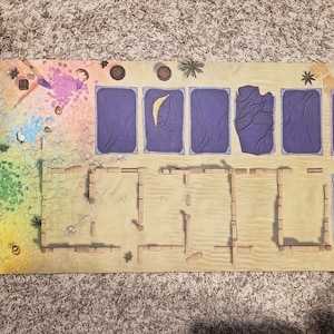 Peut inclure: Un plateau de jeu sur le th&egrave;me du d&eacute;sert. Le plateau est fait d'un mat&eacute;riau brun clair et pr&eacute;sente une vari&eacute;t&eacute; d'&eacute;l&eacute;ments color&eacute;s, notamment une tuile bleu et blanche, une tuile violette et une tuile verte. Le plateau pr&eacute;sente &eacute;galement une structure en bois avec un toit brun.