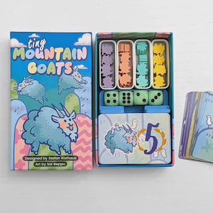 May include: A board game titled Tiny Mountain Goats with a blue box featuring cartoon goats. The open box contains four small trays with purple, orange, teal, and yellow goat tokens, four light green dice, and a deck of cards with the number 5.