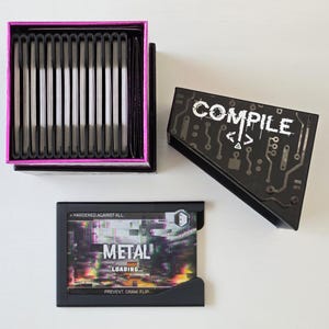May include: A black box with the word "COMPILE" in white, and a second box with the word "METAL" on it. The "COMPILE" box has a circuit board design. The "METAL" box has the words "LOADING" and "PREVENT DRAW FLIP".