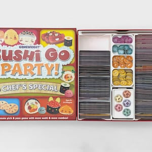 May include: Sushi Go Party! board game box and open interior tray. The box cover features cartoon sushi illustrations and the text Sushi Go Party! Chef's Special. The interior tray contains stacks of cards and small circular tokens in various colors.