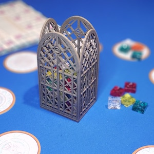 May include: A gray wooden box with a lattice design, filled with colorful glass gems. The box is sitting on a blue surface with several other colorful glass gems scattered around it.