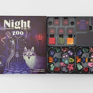 May include: A board game titled Night at the Zoo with a dark purple box cover featuring a wolf, a leopard, and a gate. The open box contains a black plastic insert with various small colored animal-shaped tokens and square game tiles.