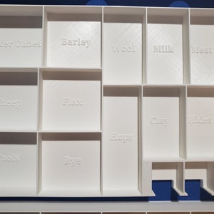 May include: A white, compartmentalized organizer with labeled sections for game components. The labels include "Worker Cubes," "Barley," "Wool," "Milk," "Meat," "Sheep," "Flax," "Hops," "Clay," "Hides," "Tools," and "Rye."