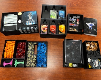 May include: A black organizer for the board game Catan: Starfarers, featuring various compartments filled with game pieces, cards, and dice. The game pieces are in various colors, including orange, red, blue, and gold. The game box is visible.