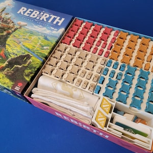 May include: Open board game box titled "Rebirth". The box reveals game pieces in red, tan, orange, and blue. A folded cloth and other game components are also visible within the box.