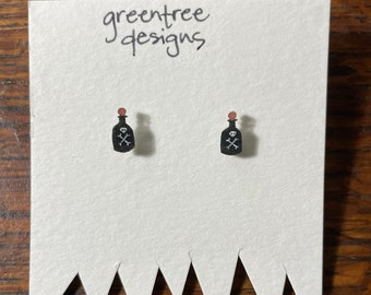 May include: A pair of black poison bottle earrings with a skull and crossbones design. The earrings are on a white card with the text "greentree designs".