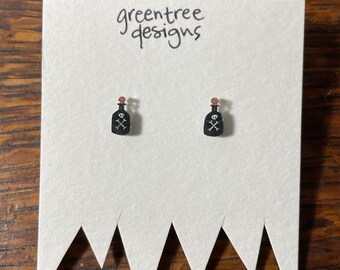 May include: A pair of black and white poison bottle earrings with a skull and crossbones design. The earrings are on a white card with the text "greentree designs".