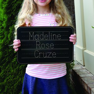 Puede incluir: Una pizarra negra con l&iacute;neas blancas y un marco dorado. La pizarra tiene el nombre "Madeline Rose Cruze" escrito en ella.