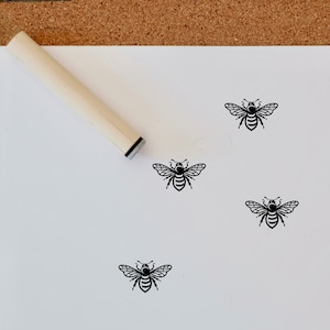 May include: Four black and white bee stamps on a white background. A wooden stamp handle is also visible in the image.