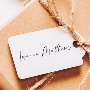 May include: A white gift tag with the name "Lauren Matthews" written in black cursive script. The tag is tied to a brown package with twine.