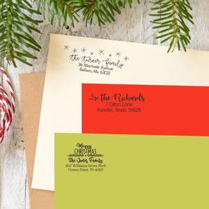 May include: Three Christmas-themed return address stamps with different designs. The top stamp is white with black text and stars, reading "the turner family 36 Montvale Avenue Ballwin, Mo 63021". The middle stamp is red with black text and holly, reading "the Richards 7 Ditton Lane Kerrville, Texas 78028". The bottom stamp is green with black text and holly, reading "Merry CHRISTMAS The Jones Family 1947 Williams Grove Blvd. Crown Point, IN 46307".