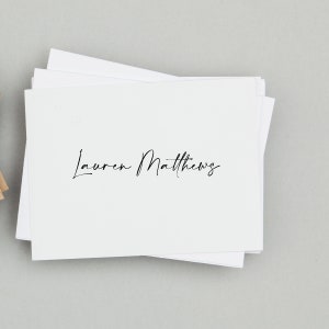 May include: A stack of white note cards with the name "Lauren Matthews" written in black cursive.