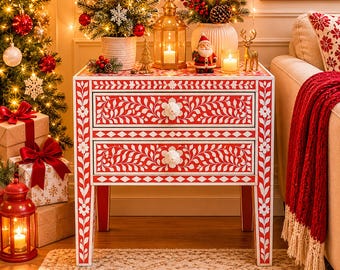 May include: A red and white floral patterned two-drawer side table. The table has a white floral design on a red background. The drawers have white flower-shaped knobs. The table is decorated with Christmas ornaments and a small Christmas tree.