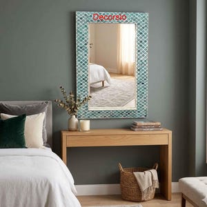 May include: A rectangular wall mirror featuring a frame with a teal and white fish scale pattern and the text Decorsio at the top. The mirror reflects a bedroom interior with a bed and curtains, providing a clear view of the decorative frame design.