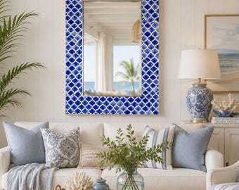 May include: A rectangular wall mirror featuring a vibrant blue and white quatrefoil tile pattern frame. The reflective glass surface displays a clear view of a room interior with a palm tree visible through a window, reflecting light.