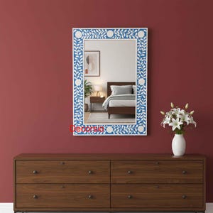 May include: A rectangular wall mirror featuring a blue and white floral inlay frame with a repeating vine and flower pattern. The mirror reflects a bedroom interior with a bed and nightstand. The word Decorsio is printed in red on the frame.