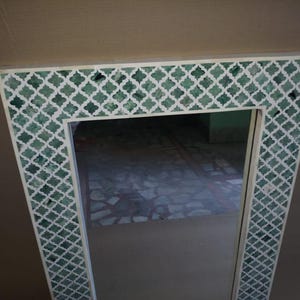 May include: A rectangular wall mirror featuring a wide frame with a white and green quatrefoil pattern. The frame consists of white lattice work inlaid over a deep green background, creating a repeating geometric design around the central glass.