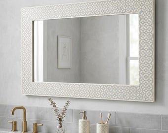 May include: A rectangular wall mirror featuring a wide frame with a repeating white and light grey geometric circular pattern. The mirror has a reflective glass surface that shows a partial view of a bathroom interior with a sink and accessories.