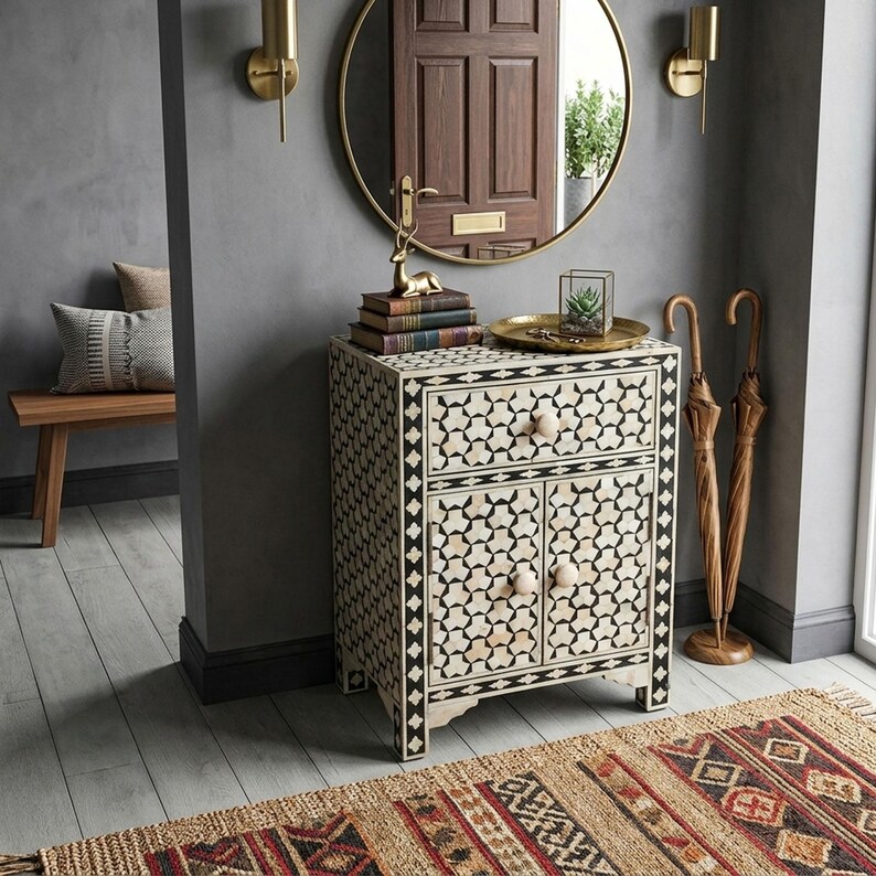 A rectangular cabinet featuring a black and white geometric inlay pattern, one top drawer, and two lower doors with round wooden knobs. The cabinet is constructed with a frame-like border and stands on four short, straight legs.