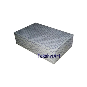 Può includere: Una scatola di immagazzinaggio rettangolare con una base bianca e un motivo geometrico viola. La scatola è in legno e ha una finitura liscia. Il testo "TakshviArt" è stampato sul fondo della scatola.