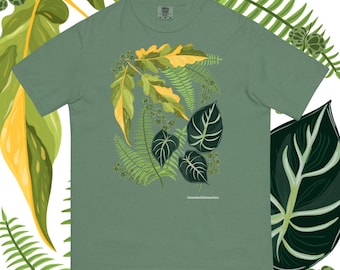 May include: A sage green t-shirt featuring a botanical illustration of various leaves in shades of green and yellow. The design includes fern-like leaves and larger, patterned leaves. The text "amandabellalmanza" is printed at the bottom of the design.