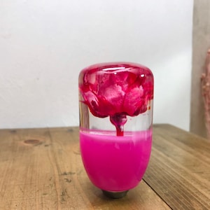 Könnte beinhalten: Ein pinkfarbener und transparenter Schaltknauf aus Harz mit einer rosa Blume im Inneren.
