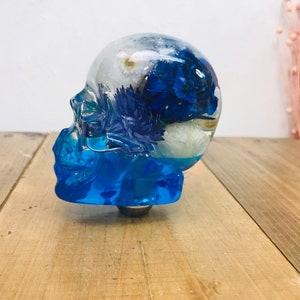 Könnte beinhalten: Ein blauer und weißer Schädel aus Harz mit getrockneten Blumen im Inneren. Der Schädel ist ein Dekorationsobjekt.