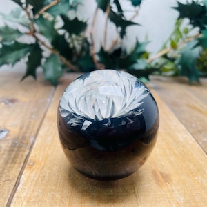 Könnte beinhalten: Ein schwarzer Glas-Briefbeschwerer mit einem in die Oberfläche geschnitzten weißen Blumendesign.